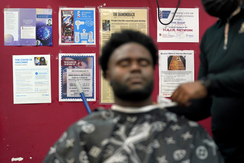 Health literature and a certificate are displayed on the wall as a patron gets a hair cut, Friday, April 9, 2021, in Hyattsville, Md. Barbers at The Shop are members of the Health Advocates In Reach & Research (HAIR) program, which helps barbers and hair stylists to get certified to talk to community members about health. During the COVID-19 pandemic, a team of certified barbers have been providing factual information to customers about vaccines, a topic that historically has not been trusted by members of black communities because of the health abuse the race has endured over the years. (AP Photo/Julio Cortez)