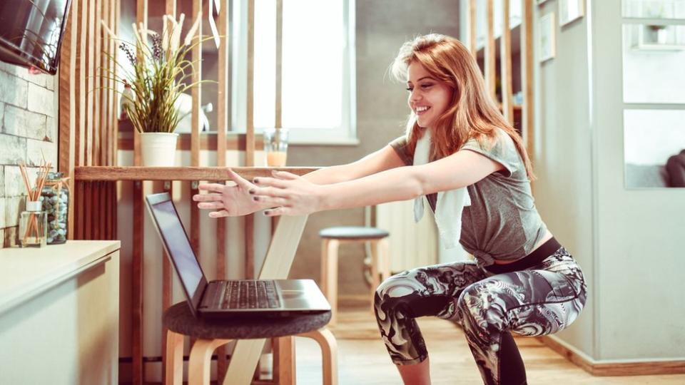 Una mujer haciendo sentadillas frente a una laptop.