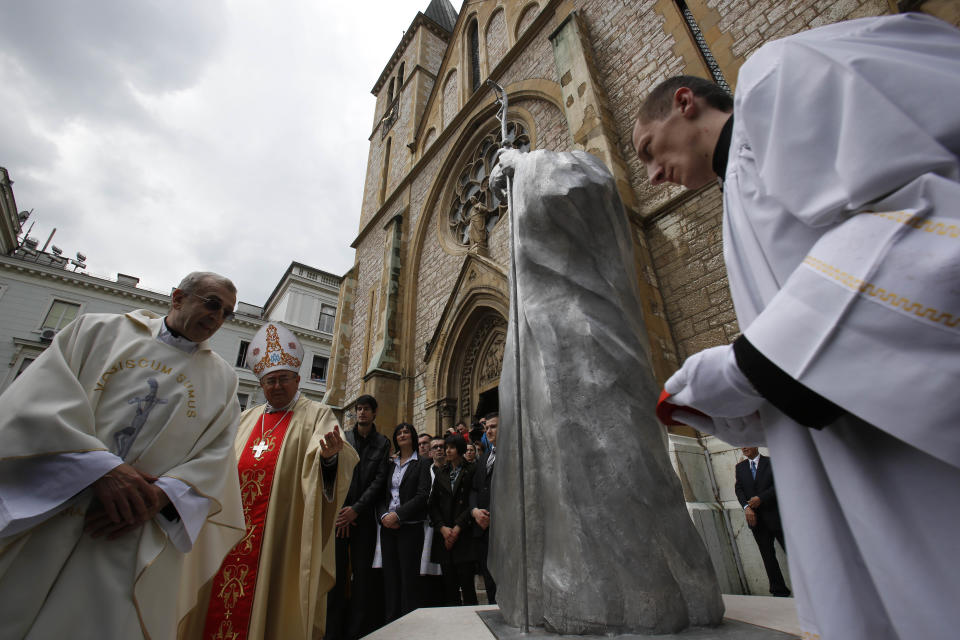 Bosnian Cardinal Vinko Puljic, second left, and Franjo Topic, left, Head of the Croat Cultural association 'Napredak', unveils the statue of Pope John Paul II in front of the cathedral in Sarajevo, Bosnia, on Wednesday, April 30, 2014. Thousands of Bosnians have celebrated the canonization of Pope John Paul II by unveiling a statue in the heart of Sarajevo. John Paul’s support for Sarajevo's resistance to nationalist efforts to destroy the traditional inter-cultural and inter-religious fabric of the city during the 1992-95 war made him very popular among the city's predominantly Muslim population. The crowd shouted “long live the pope” as the three meter-high statue was unveiled Wednesday in front of the cathedral. (AP Photo/Amel Emric)