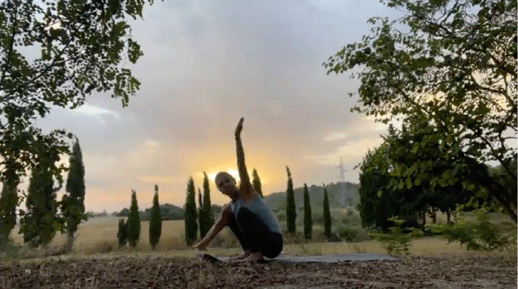 Woman practicing yoga on a mat outside at sunrise