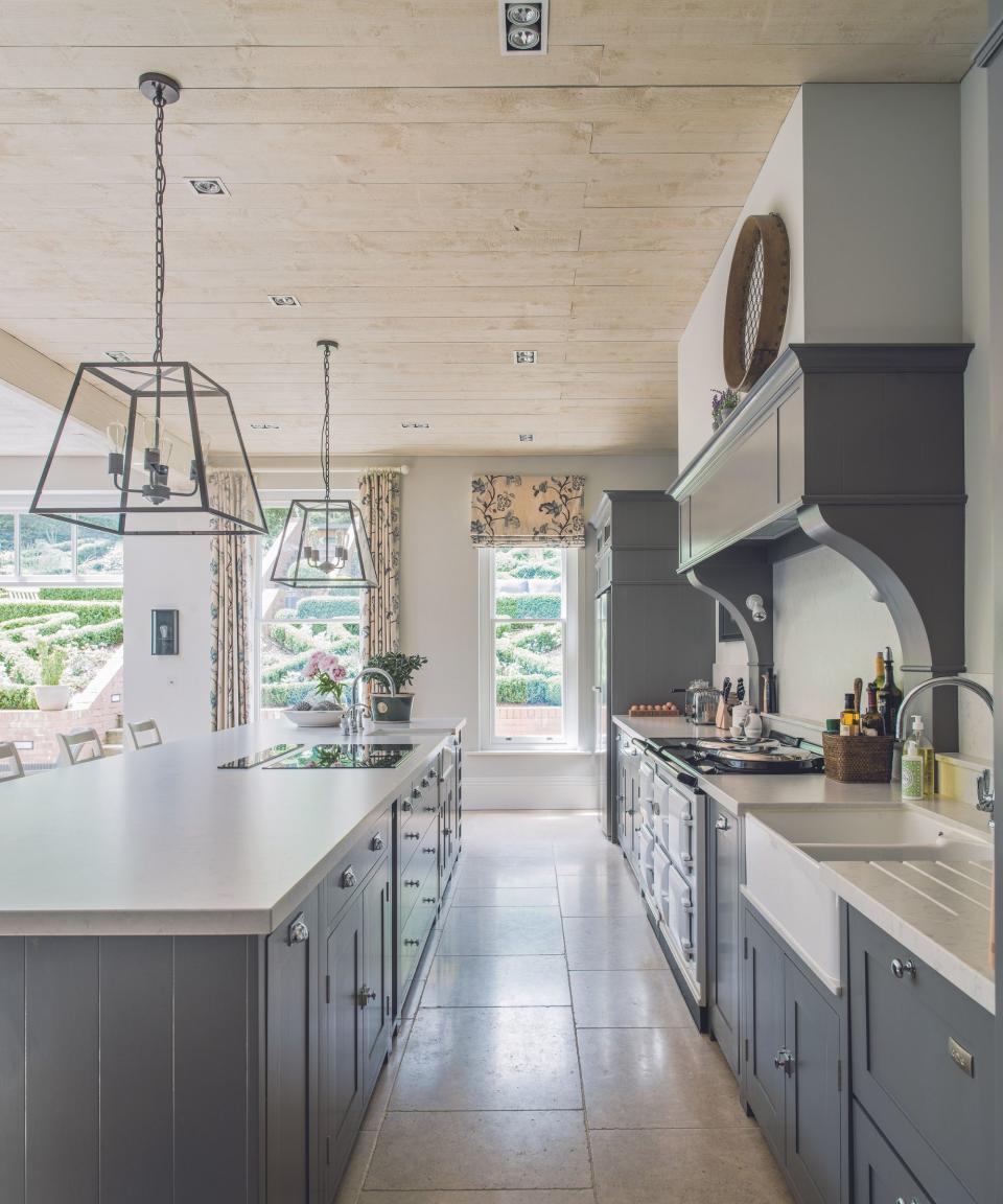 Kitchen with grey fitted kitchen cupboards and kitchen island with white worktop and tiled floor.