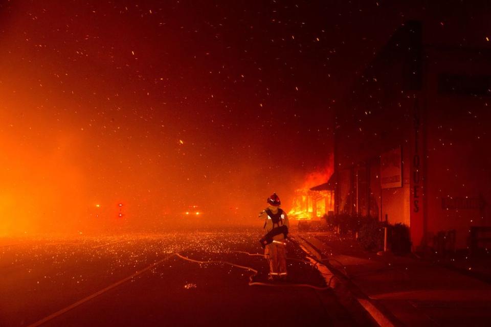 A fire fighter stands at the ready to protect a building across the street, as the Camp Fire burned out of control through Paradise, fueled by high winds in Butte County, Calif., on Nov. 8, 2018.