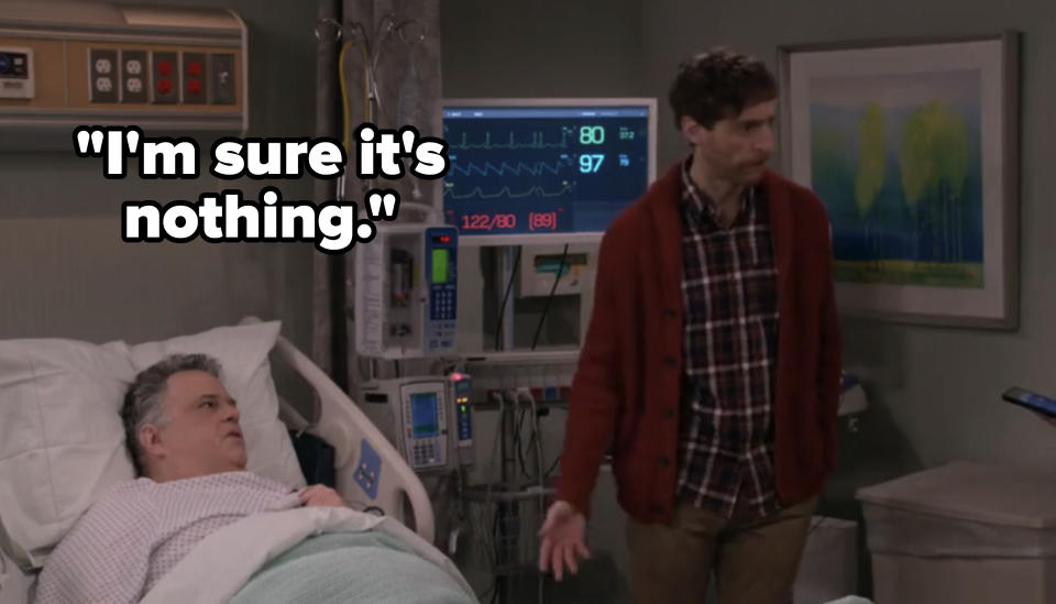 Two TV show characters in a hospital room, one lying in bed and the other standing with a concerned expression
