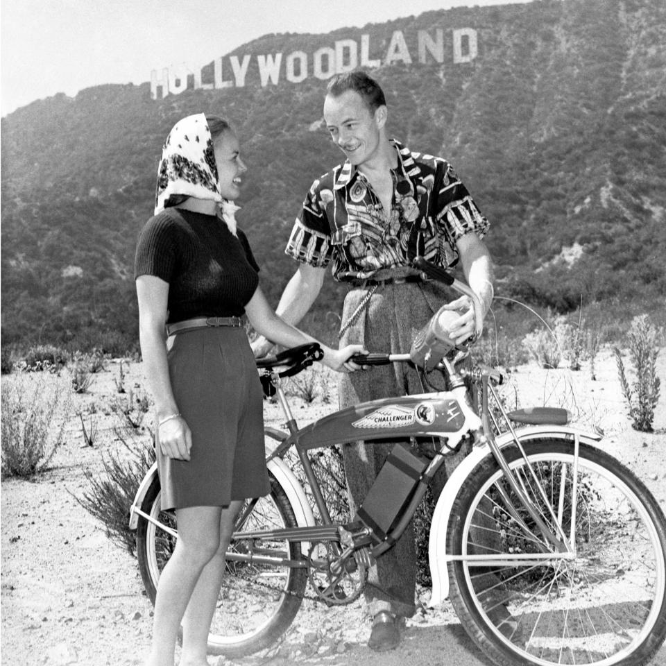 Les Tremayne, of CBS Radio's "First Nighter" program, and wife (the former Eileen Palmer), with their bicycles in the Hollywood Hills, with the Hollywoodland sign in the background; August 3, 1940.