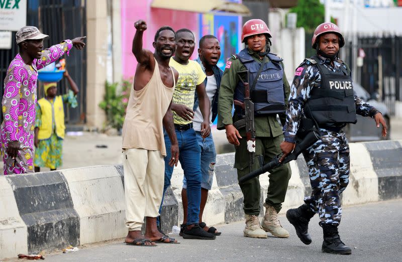 Men gesture as they stand near police officers along a street in Ikeja, in Lagos