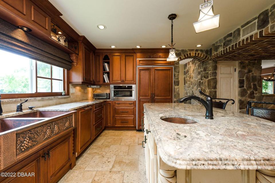The amazing, Tuscan-style kitchen is adorned with brick-and-stone accents, a large copper farmhouse sink, custom cabinetry and counters, a six-burner, gas Wolf range and two dishwashers camouflaged into the cabinets.