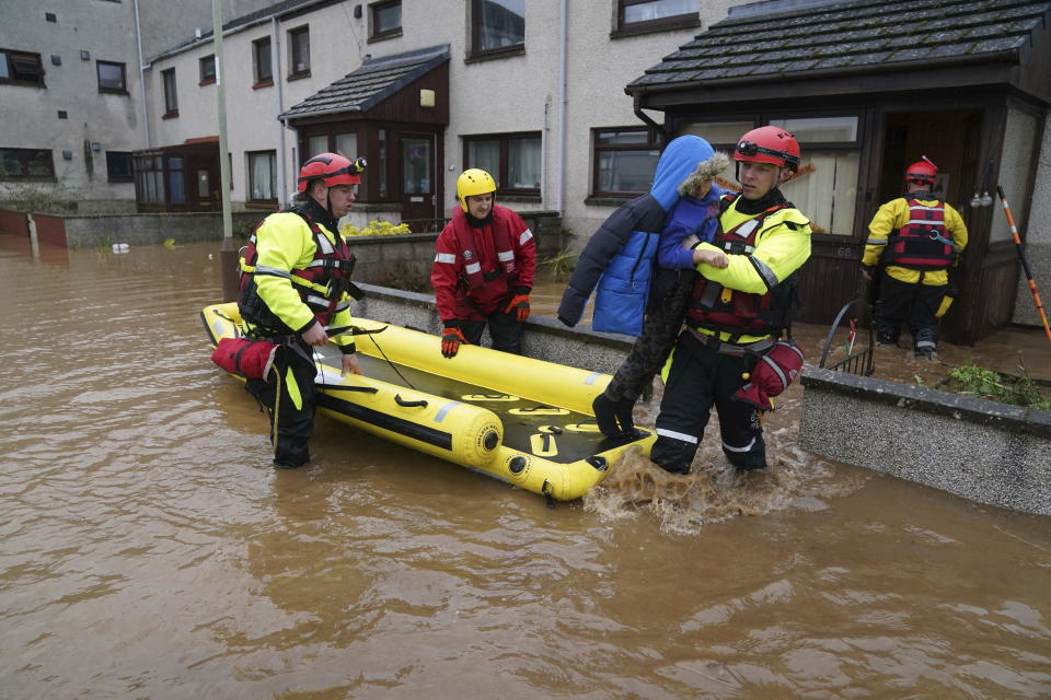 A member of the emergency services carries a boy from a house as Storm Babet batters the country, in Brechin, Scotland, Friday Oct. 20, 2023. Flood warnings are in place in Scotland, as well as parts of northern England and the Midlands. (Andrew Milligan/PA via AP)