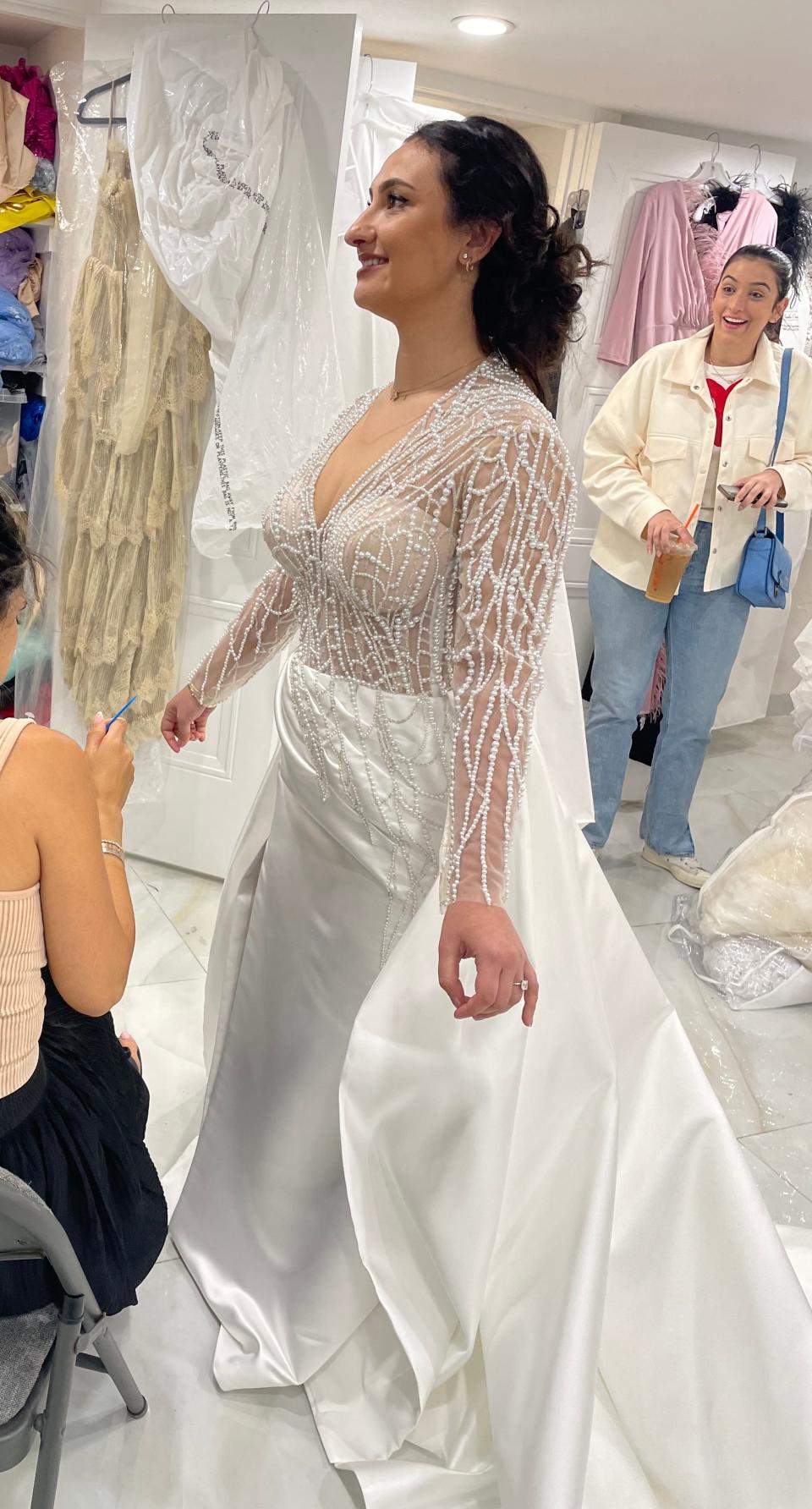 Pepa trying on the custom wedding dress, with a friend in the background staring with an open mouth at the gown