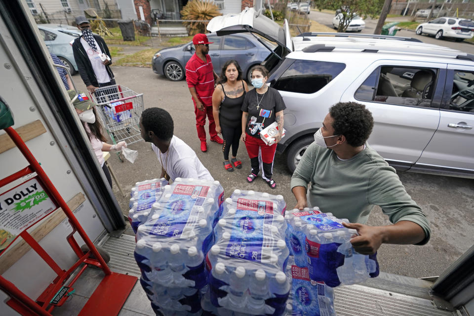 Marcel McClinton, right, hands out cases of donated water to residents affected by a severe winter storm, Friday, Feb. 26, 2021, in Houston. Local officials, including Houston Mayor Sylvester Turner, say they have focused their efforts during the different disasters on helping the underserved and under-resourced but that their work is far from complete. (AP Photo/David J. Phillip)