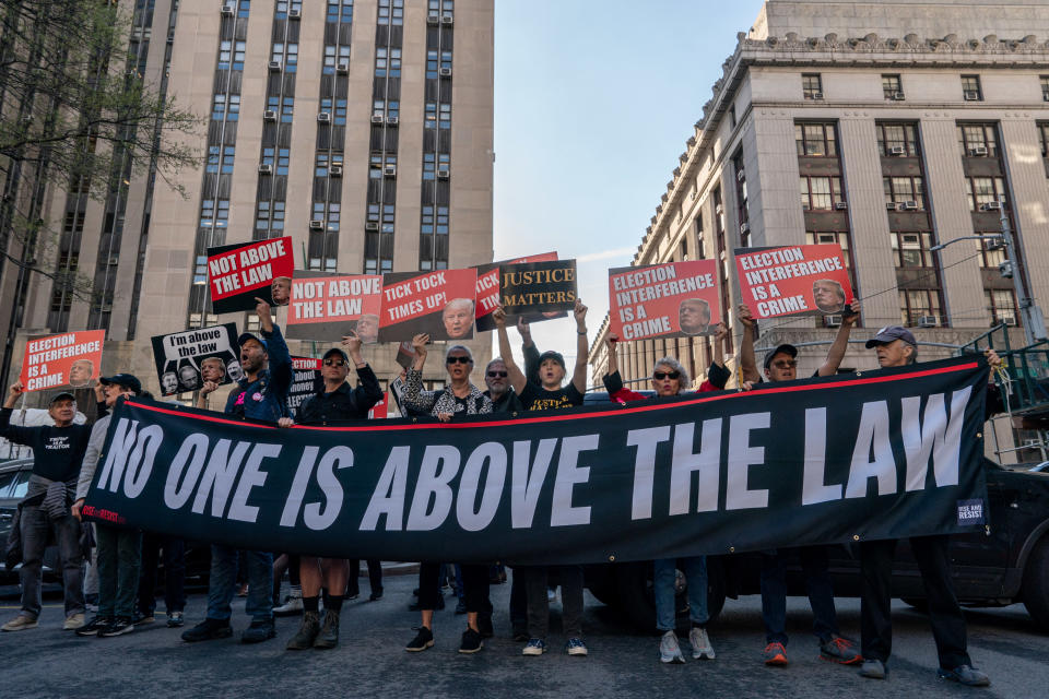 Group of people holding signs and a large banner that reads "NO ONE IS ABOVE THE LAW" during a demonstration