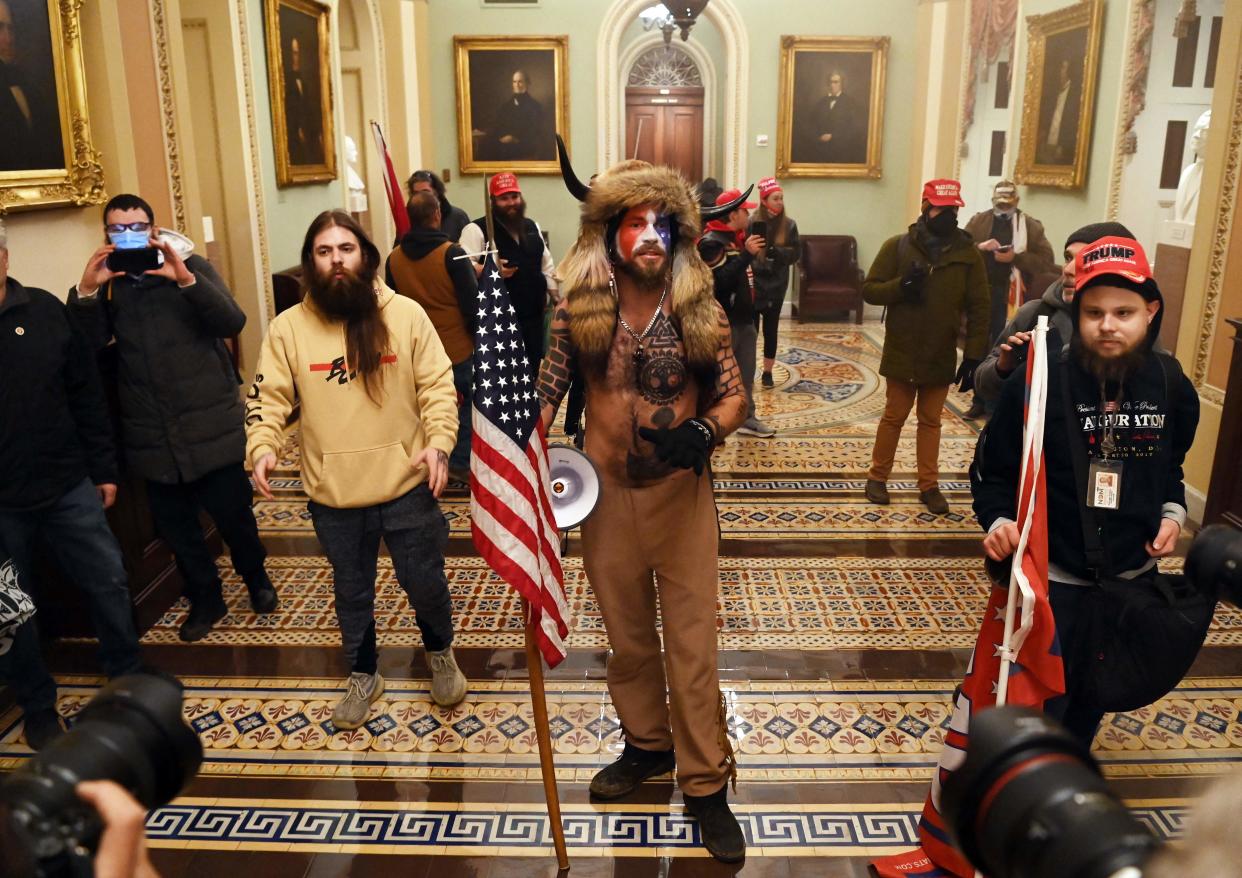 Jacob Chansley, aka the QAnon Shaman, holds the American flag inside the U.S. Capitol on Jan. 6, 2021, after a violent mob broke through police lines and tried to stop congressional certification of Joe Biden's election to the presidency. A lawyer for Donald Trump argued Thursday that the assault on the Capitol was a riot, but not an insurrection.