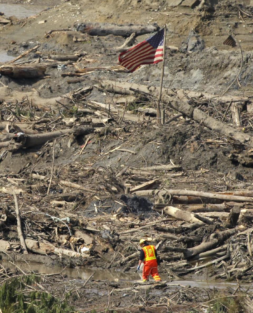 A search worker walks through a channel of water as a flag flies in the debris field Monday, March 31, 2014, near Darrington, Wash., at the site of the massive mudslide that hit the nearby community of Oso,Wash. on March 22, 2014. (AP Photo/Ted S. Warren)