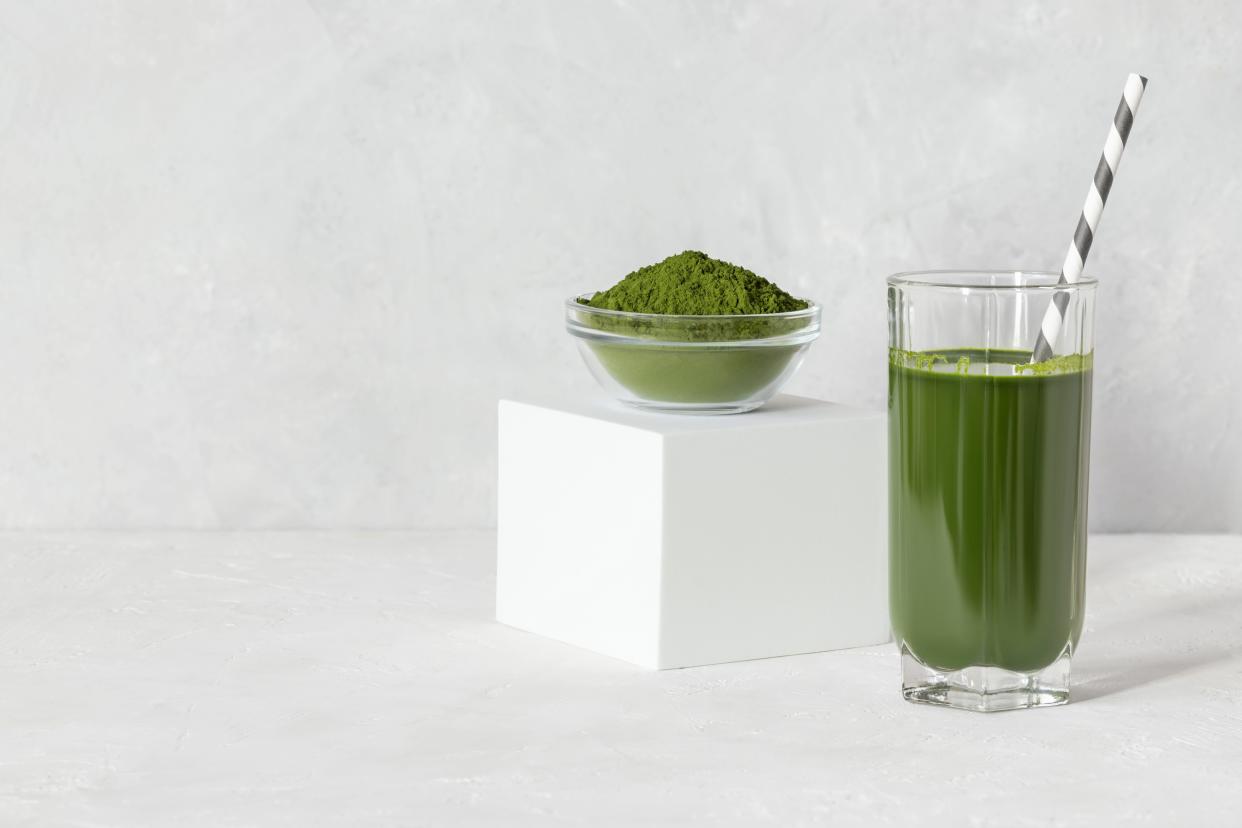 Green drink in a glass and powder on a white concrete background.