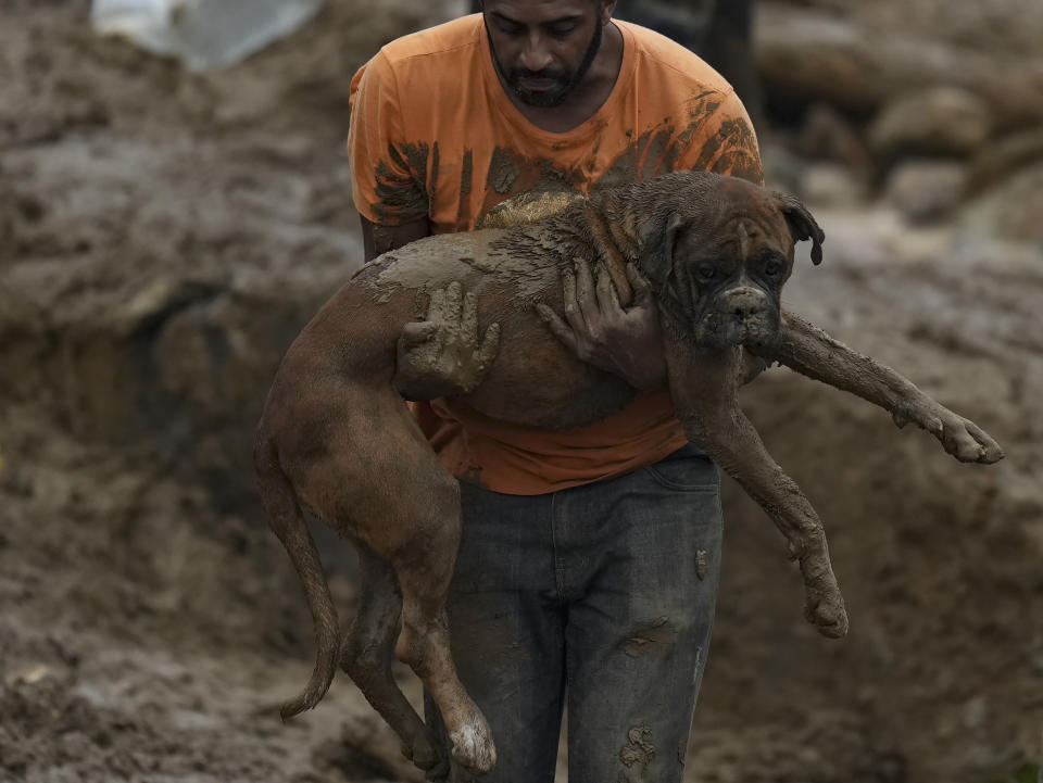 A man carries a dog rescued from a residential area destroyed by mudslides in Petropolis, Brazil, on Feb. 16, 2022. (AP Photo/Silvia Izquierdo)