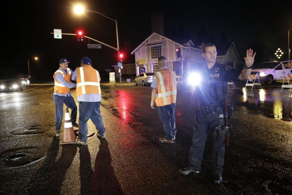 A police officer controls the traffic as workers shut off the water valve on Friday, March 28, 2014, in Fullerton, Calif. A magnitude-5.1 earthquake was widely felt in the Los Angeles area and surrounding counties Friday evening, but authorities said there were no immediate reports of significant damages or injuries. (AP Photo/Jae C. Hong)