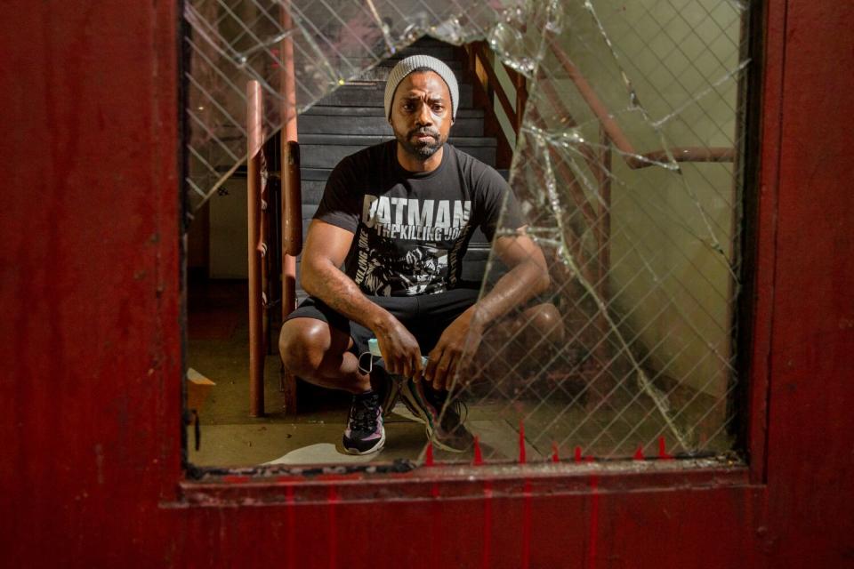 A man looks through a broken glass panel of an exit door