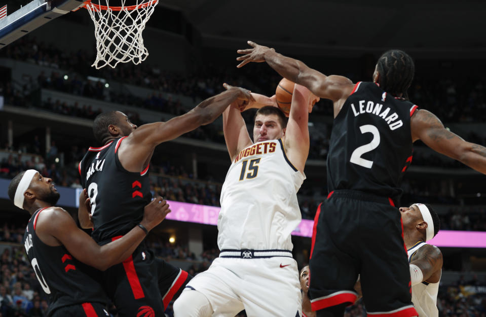 Nikola Jokic, de los Nuggets de Denver, atrapa un rebote frente a CJ Miles (izquierda), Serge Ibaka y Kawhi Leonard (2), de los Raptors de Toronto, el domingo 16 de diciembre de 2018 (AP Foto/David Zalubowski)