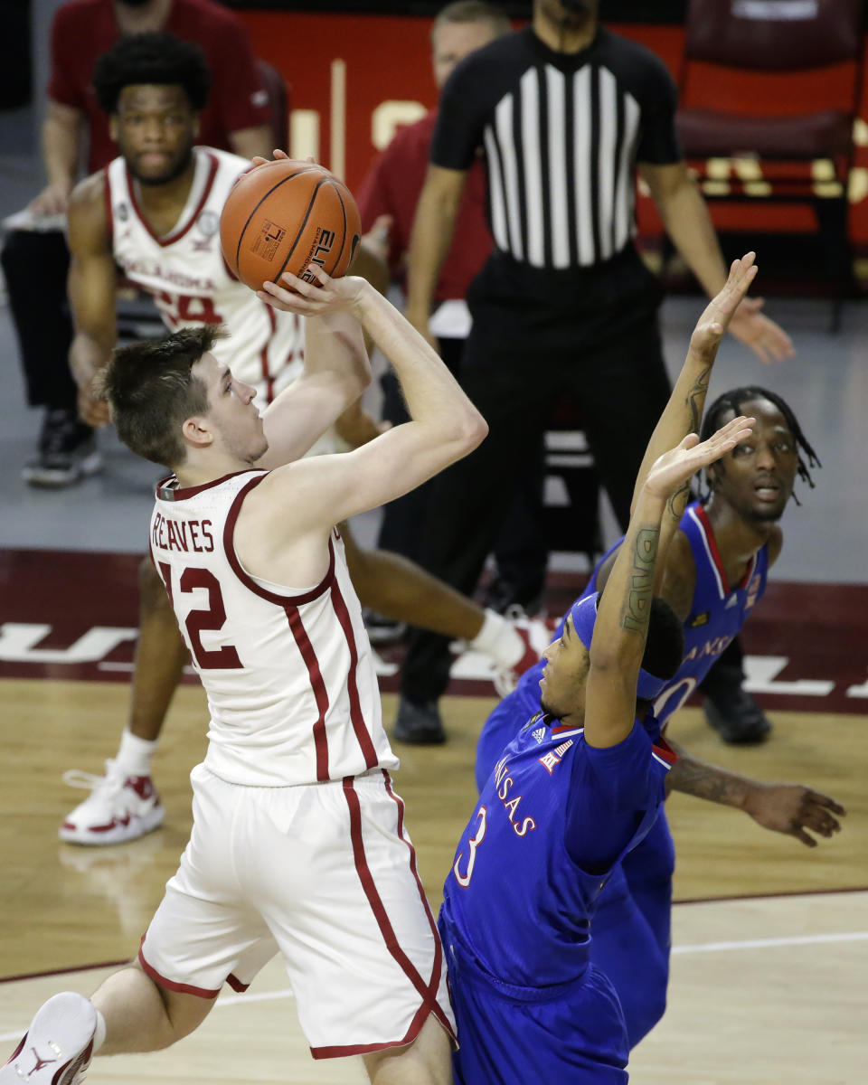 Oklahoma guard Austin Reaves (12) takes a shot against Kansas guard Dajuan Harris (3) while Oklahoma guard Elijah Harkless (24) and Kansas guard Marcus Garrett (0) look on during the second half of an NCAA college basketball game in Norman, Okla., Saturday, Jan. 23, 2021. (AP Photo/Garett Fisbeck)