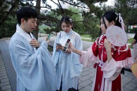 Young people dressed in "Hanfu" use their mobile devices at an event marking the traditional Qixi festival, at a park in Beijing, China