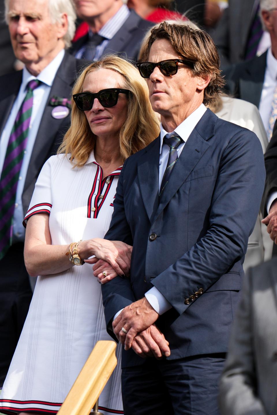 Julia Roberts and Daniel Moder attending an event, wearing sunglasses. Julia is in a casual dress while Daniel wears a formal suit