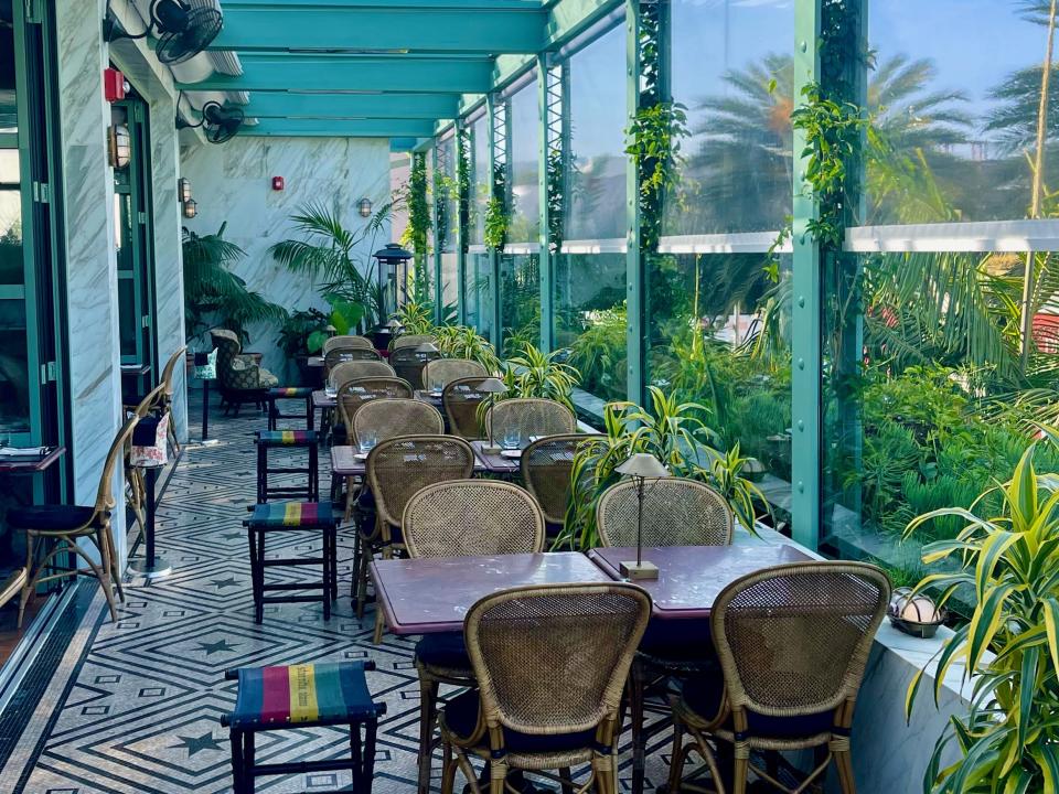 A restaurant with an enclosed terrace with turquoise colors, mosaic floors, and wicker chairs.