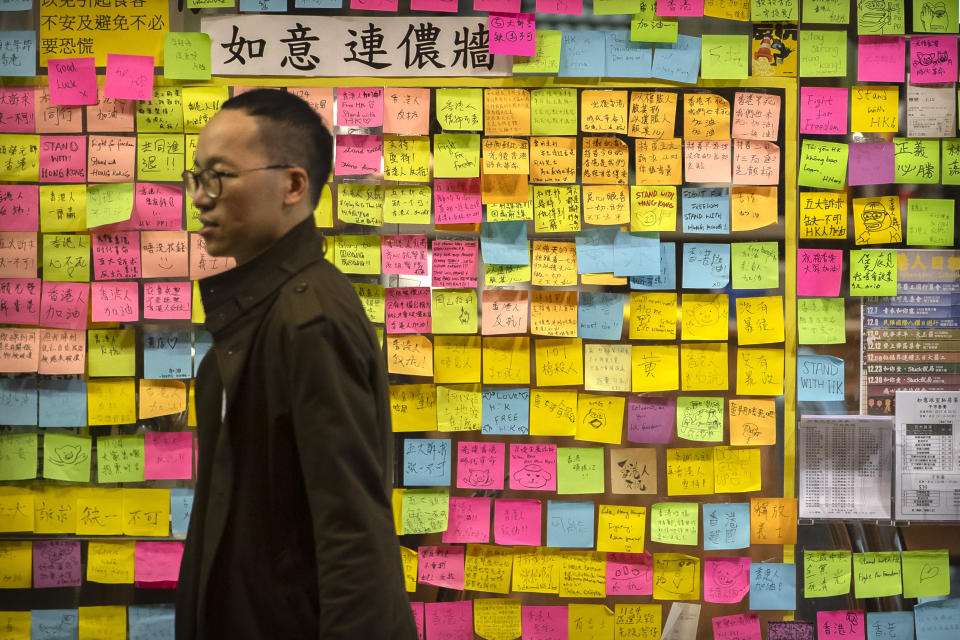 In this Monday, Dec. 16, 2019 photo, people walk past the entrance of a tea shop that has been turned into a "Lennon wall" of pro-protest notes in Hong Kong. Stores that have come out in open support of Hong Kong's pro-democracy protest movement, nicknamed "yellow shops," make their politics plain and are winning customers in protest-hit Hong Kong because it. (AP Photo/Mark Schiefelbein)