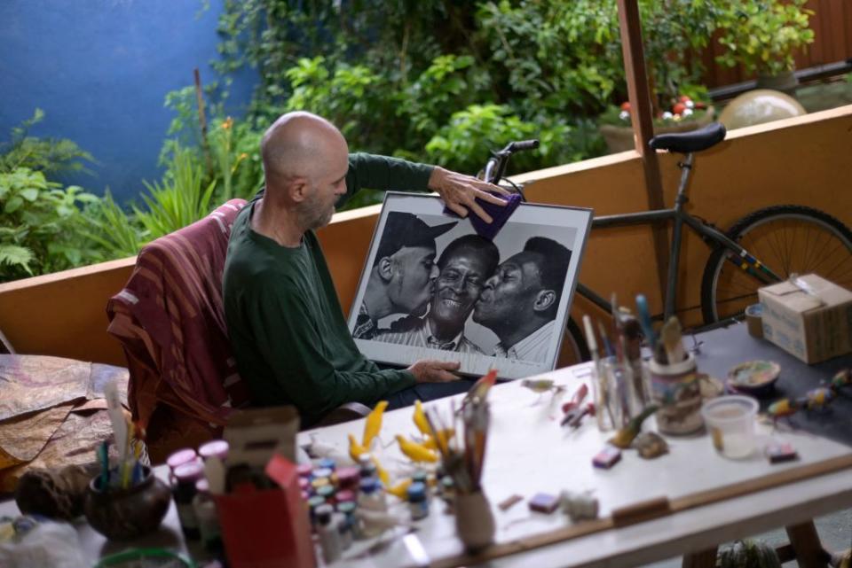 Fernando Ortiz, friend and representative of Brazil's football legend Edson Arantes do Nascimento 'Pele', cleans a picture of Pele (R) with his father Dondinho (C) and son Edinho, at his house in the footballer's hometown Tres Coracoes, state of Minas Gerais, Brazil, on December 28, 2022. - Pele, 82, is battling worsening cancer as well as kidney and heart problems at a Sao Paulo hospital. (Photo by DOUGLAS MAGNO / AFP) (Photo by DOUGLAS MAGNO/AFP via Getty Images)