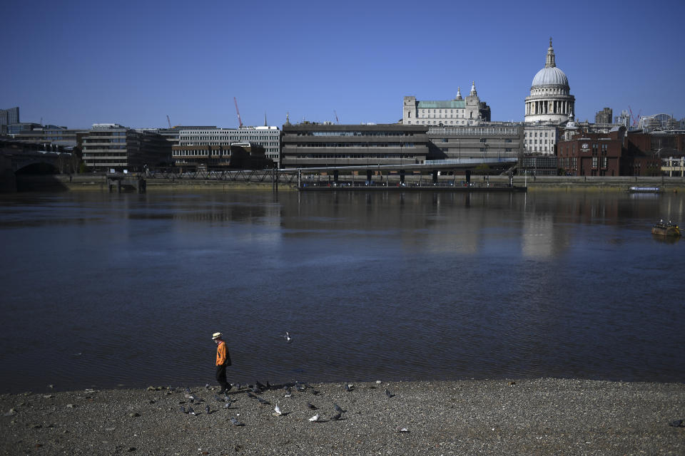 A man walks on the sand, on the south bank of the river Thames, with St. Paul's Cathedral in background right, in London, Tuesday, April 14, 2020. The new coronavirus causes mild or moderate symptoms for most people, but for some, especially older adults and people with existing health problems, it can cause more severe illness or death.(AP Photo/Alberto Pezzali)