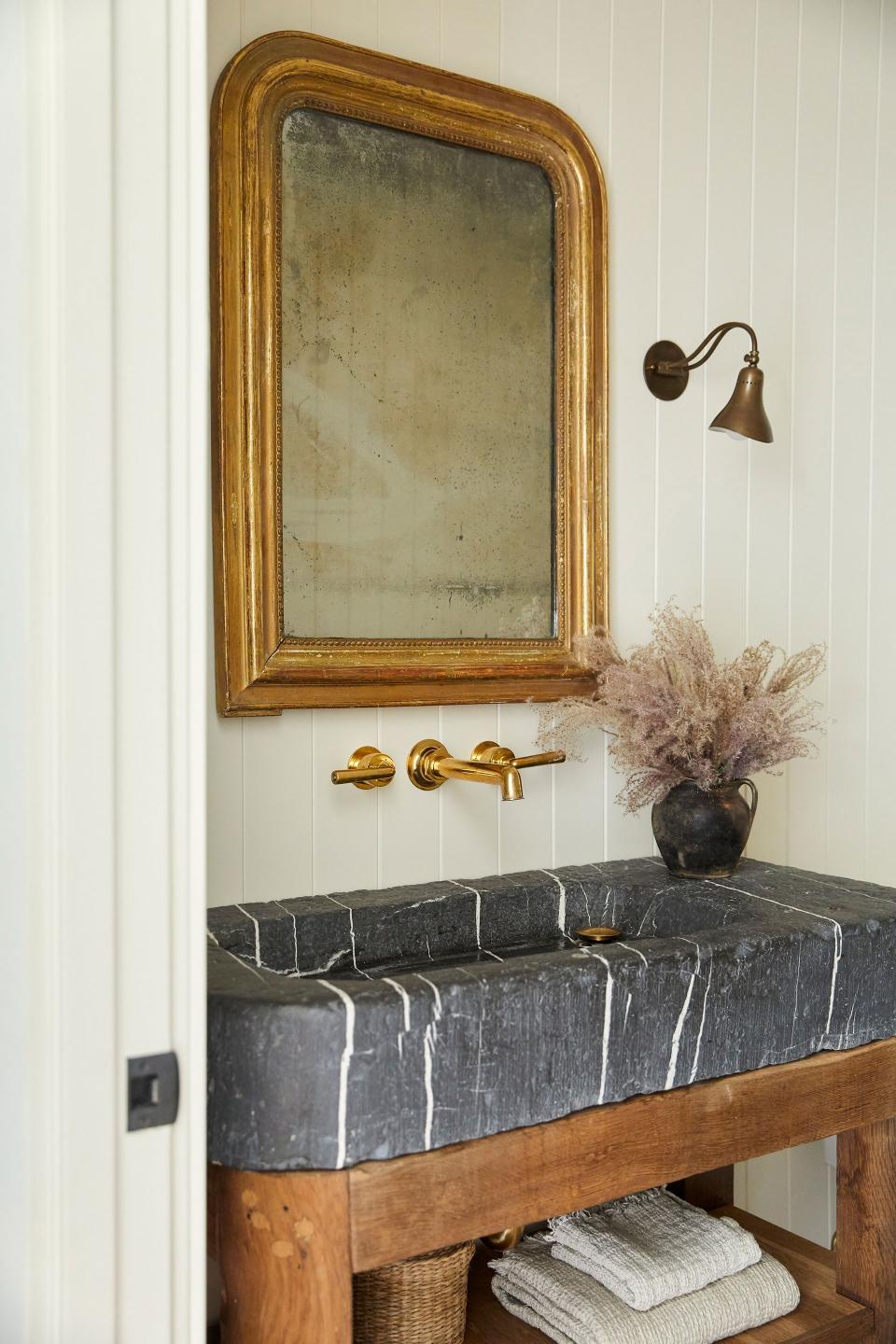 Lewis stored the powder room’s vintage French mirror in her studio’s warehouse after finding the piece in Round Top, saving it for the right home. “The patina is by design,” says Lewis. “Everybody looks pretty in that mirror.” All of the curves in the room—like the vintage trough-like stone sink from Belgium and brass sconces—open up the narrow space.