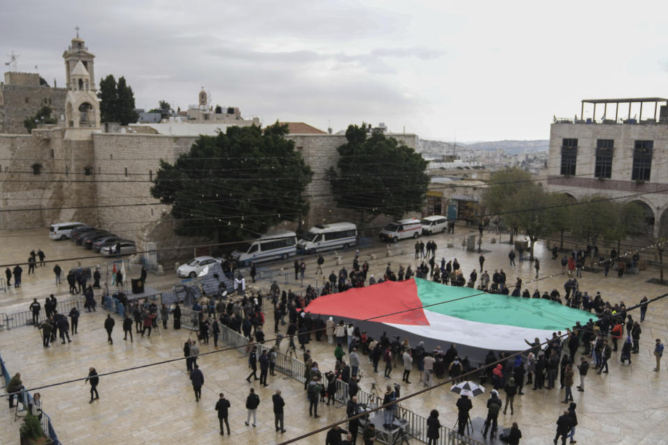 People hold a giant Palestinian flag in Manger Square, near the Nativity Church, which is traditionally believed to be the birthplace of Jesus, on Christmas Eve, in the West Bank city of Bethlehem, Sunday, Dec. 24, 2023. Bethlehem is having a subdued Christmas after officials in Jesus' traditional birthplace decided to forgo celebrations due to the Israel-Hamas war. (AP Photo/Mahmoud Illean)