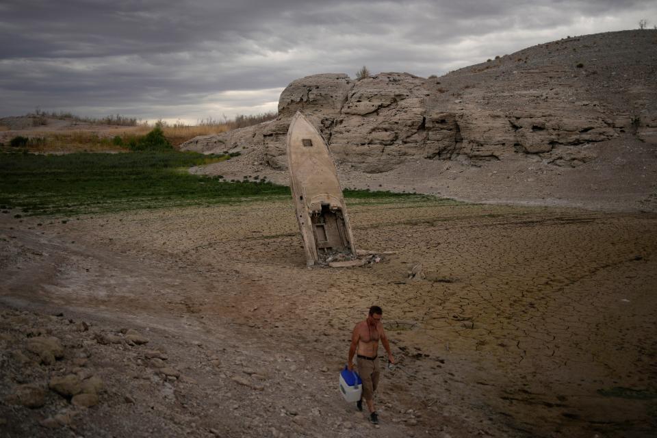 A man walks by a formerly sunken boat standing upright into the air with its stern buried in the mud along the shoreline of Lake Mead at the Lake Mead National Recreation Area near Boulder City, Nev., June 22, 2022.