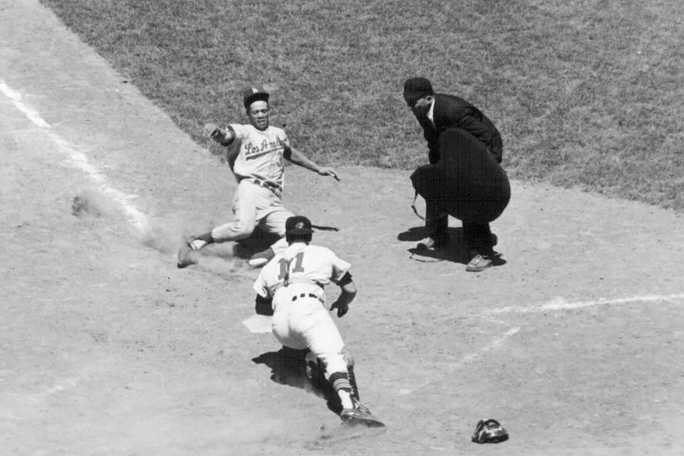 FILE - Los Angeles Dodgers' Maury Wills slides safely home past under American League catcher John Romano of the Cleveland Indians, to score in this eighth inning of the baseball All-Star game in Washington, July 10, 1962. Maury Wills, who helped the Los Angeles Dodgers win three World Series titles with his base-stealing prowess, has died. The team says Wills died Monday night, Sept. 19, 2022, in Sedona, Ariz. He was 89. (AP Photo/File)