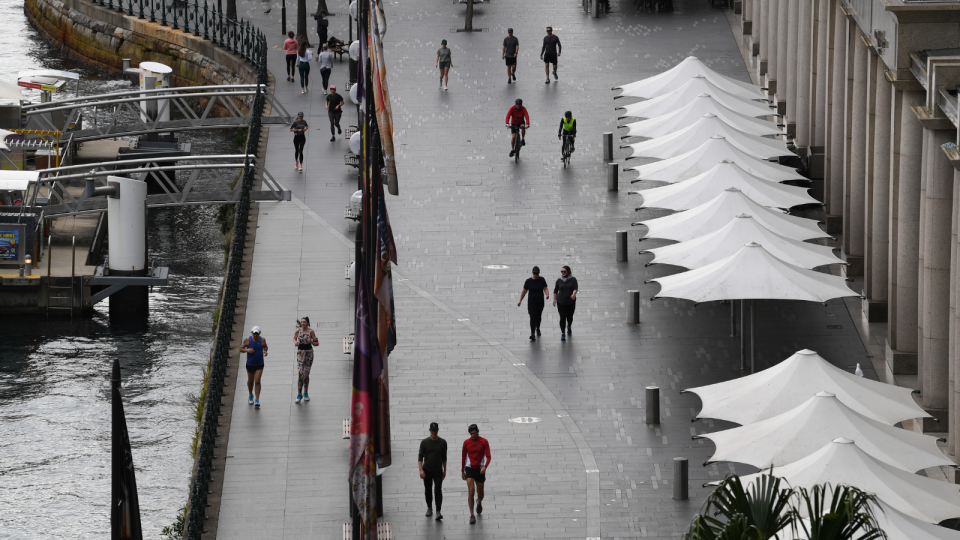 People walk in pairs by the harbour in Sydney on an overcast day.