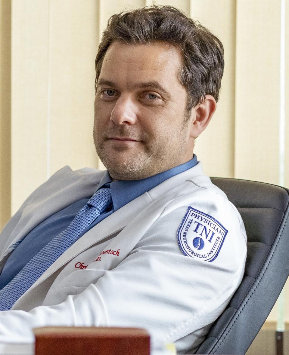 Joshua in an office chair with short hair wearing a physician's coat