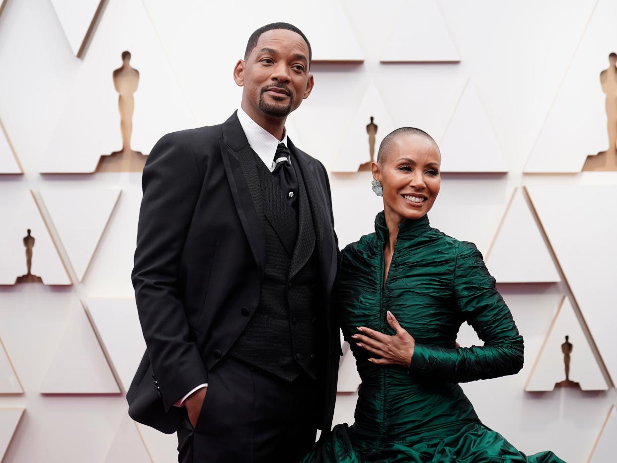 Will in a black suit and Jada in a shiny green long sleeve dress.
