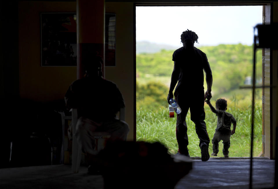 Huge Andrew and his son, Hile Andrew, 2, step out of the Rastafari tabernacle during service on Sunday, May 14, 2023, on the Ras Freeman Foundation for the Unification of Rastafari property in Liberta, Antigua. (AP Photo/Jessie Wardarski)