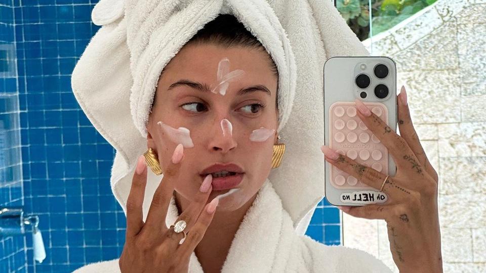 Hailey Bieber in a dressing gown and towel applying face cream