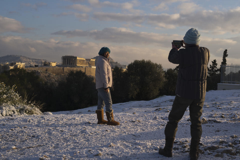 A tourist poses for a picture at Filopappos hill as at the background is seen the ancient Acropolis hill with the 500BC Parthenon temple, after snowfall in Athens, on Tuesday, Jan. 8, 2019. (AP Photo/Petros Giannakouris)