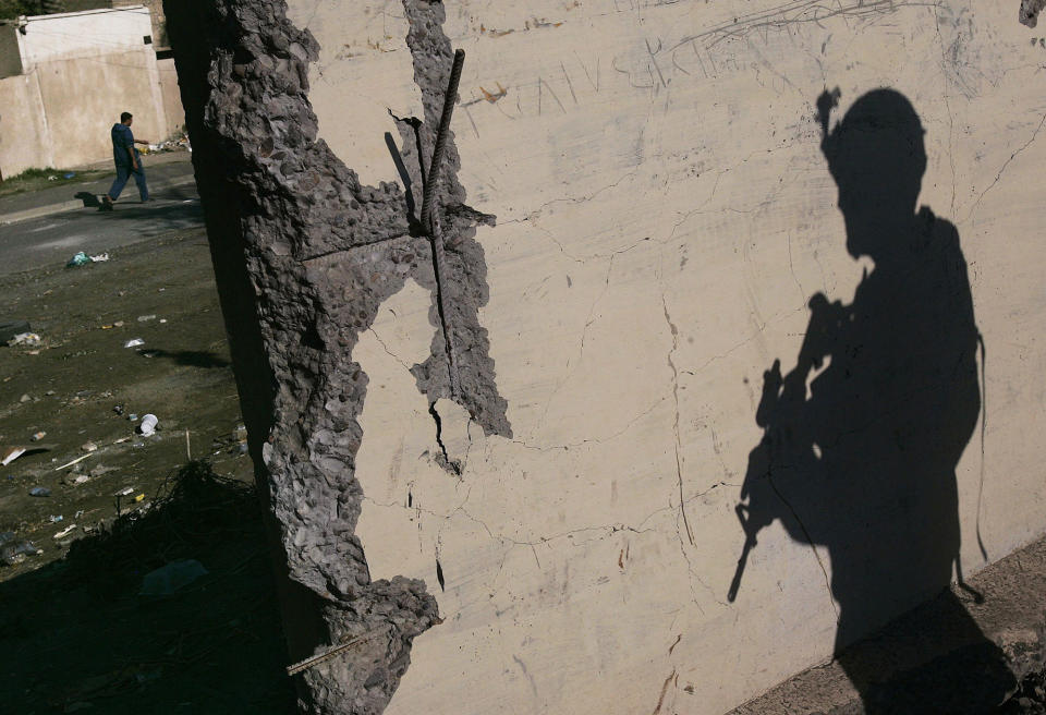 <p>A US Army soldier with Task Force Dagger stands watch while a man passes by in the distance on December 1, 2006 in the Hurriyah neighborhood of Bagdhad, Iraq. Hurriyah has been the site of violent incidents in recent weeks, including alleged sectarian mosque burnings and the killing of an U.S. Army colonel by a roadside bomb, one of the highest ranking American deaths in the Iraq war. (Photo by Chris Hondros/Getty Images) </p>