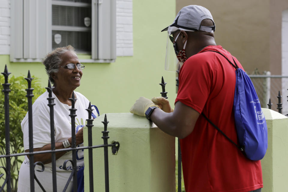 Morris Copeland, a team member of the Strategic Urban Response to Guideline Education (SURGE) group, right, talks with Louise Wilkerson, left, as he distributes kits to provide information to residents living in COVID-19 hotspots, during the new coronavirus pandemic, Wednesday, July 1, 2020, in the Liberty City neighborhood of Miami. The teams were formed by Miami-Dade County to help flatten the curve of the coronavirus. The kits contain masks, hand sanitizer, and information about testing locations. (AP Photo/Lynne Sladky)