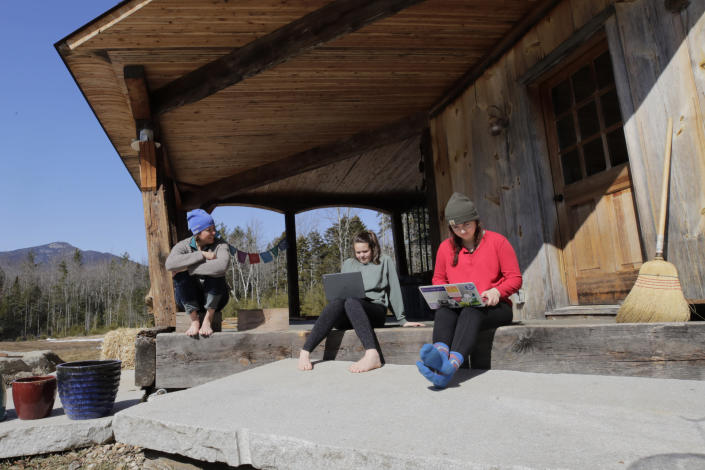 FILE - In this Thursday, March 26, 2020, file photo, Ashley Bullard, left, sits on the porch of her family's rural home in North Sandwich, N.H., as her daughters Raven, center, a senior in high school, and Willow, right, a freshman at Brandeis University, try to complete their classwork from home during the virus outbreak on a very limited internet connection. In the town of 1,200 best known as the setting for the movie "On Golden Pond," broadband is scarce. The Senate’s $1 trillion bipartisan infrastructure plan includes a $65 billion investment in broadband that the White House says will “deliver reliable, affordable, high-speed internet to every household.” (AP Photo/Charles Krupa, File)