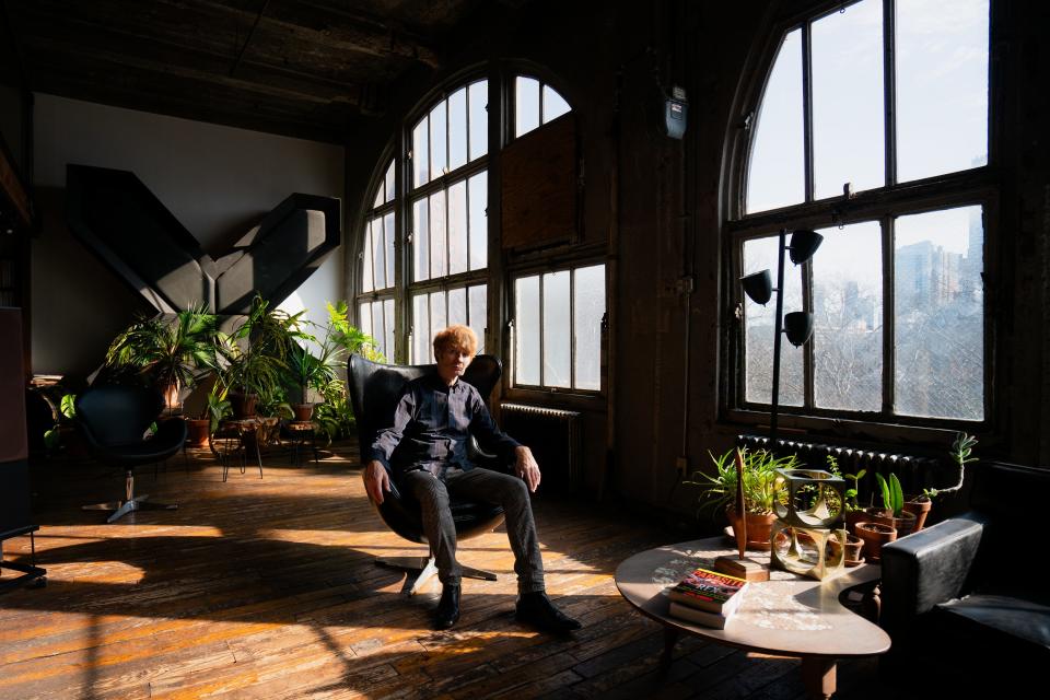 JG Thirwell sits in a modern chair surrounded by plants and massive windows in his loft.