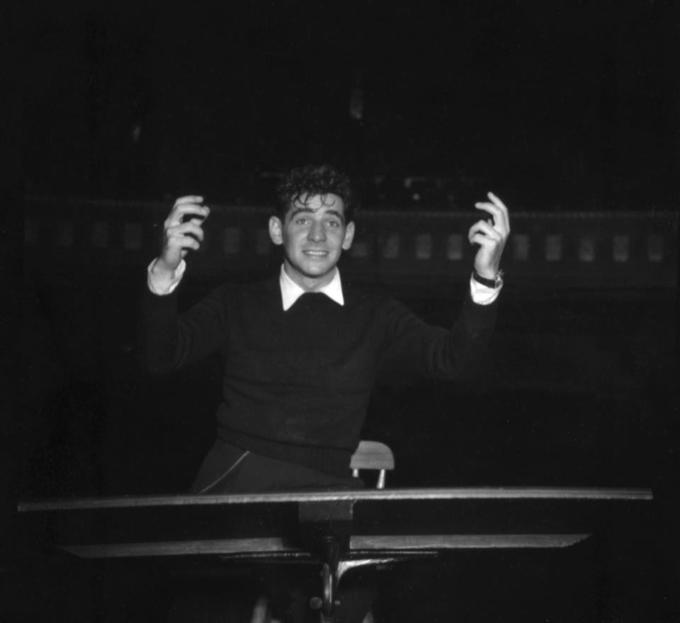 A young Leonard Bernstein, in an undated black and white photograph, conducts an orchestra.