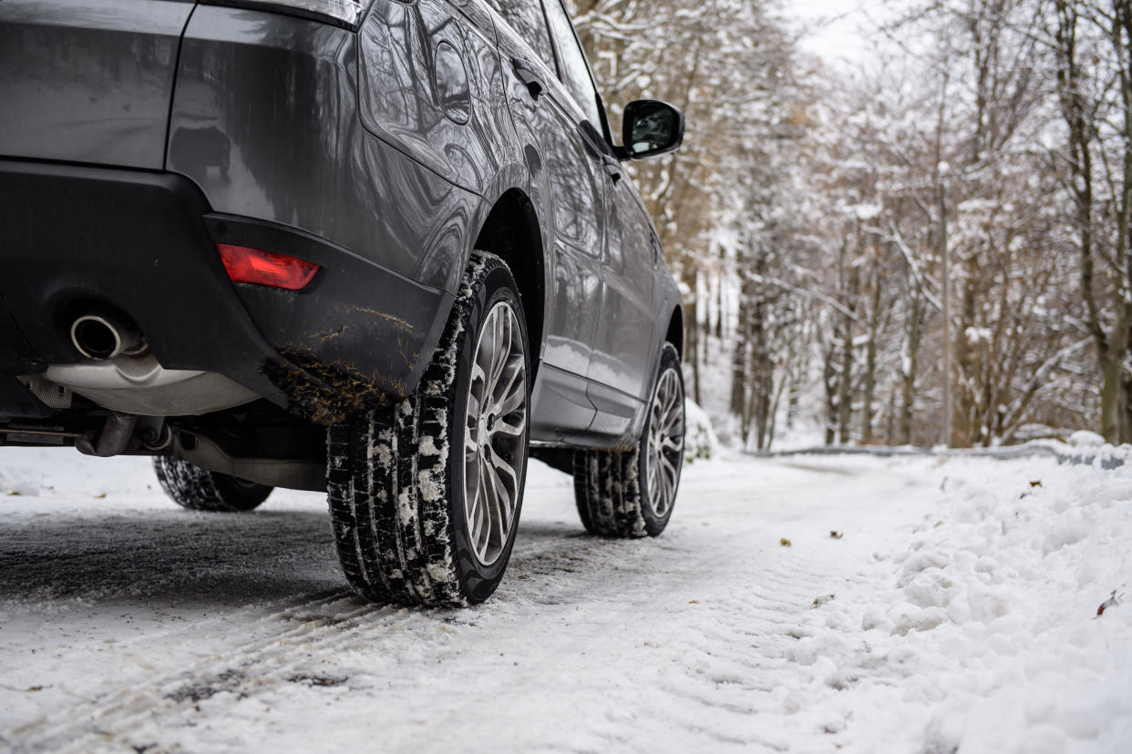 Close-up of car winter tires in a winter scenario with snow and trees in a mountain road