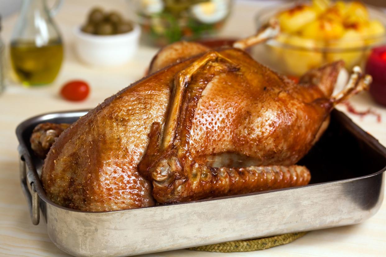 Roast goose in a baking pan with a blurred background of ingredients and food