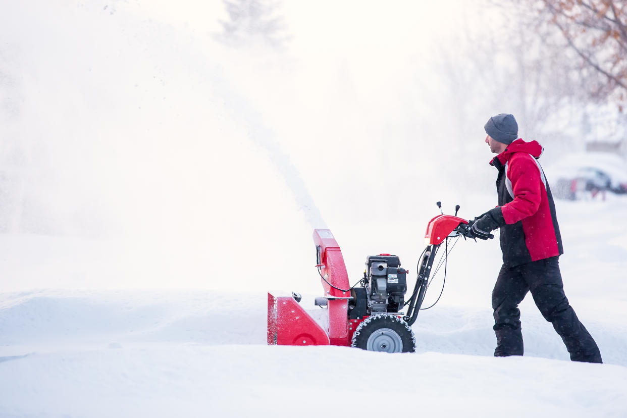 man walking with snow blower in deep white snow wearing red winter jacket, toque and black snow pants, Tackle snow removal like a pro this winter with help from a snow blower or thrower (Getty Images).