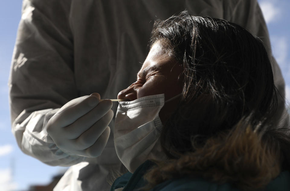 A woman grimaces as a healthcare worker collects a nasal swab sample to test for COVID-19, in Bogota, Colombia, Wednesday, Jan. 27, 2021. The Colombian government announced that the first shipment of new coronavirus vaccines will arrive in February. (AP Photo/Fernando Vergara)