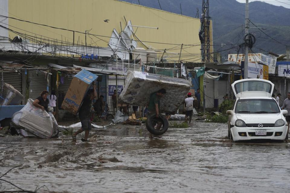 People carry away a mattress, a television monitor and a bicycle from a store at a shopping mall after Hurricane Otis