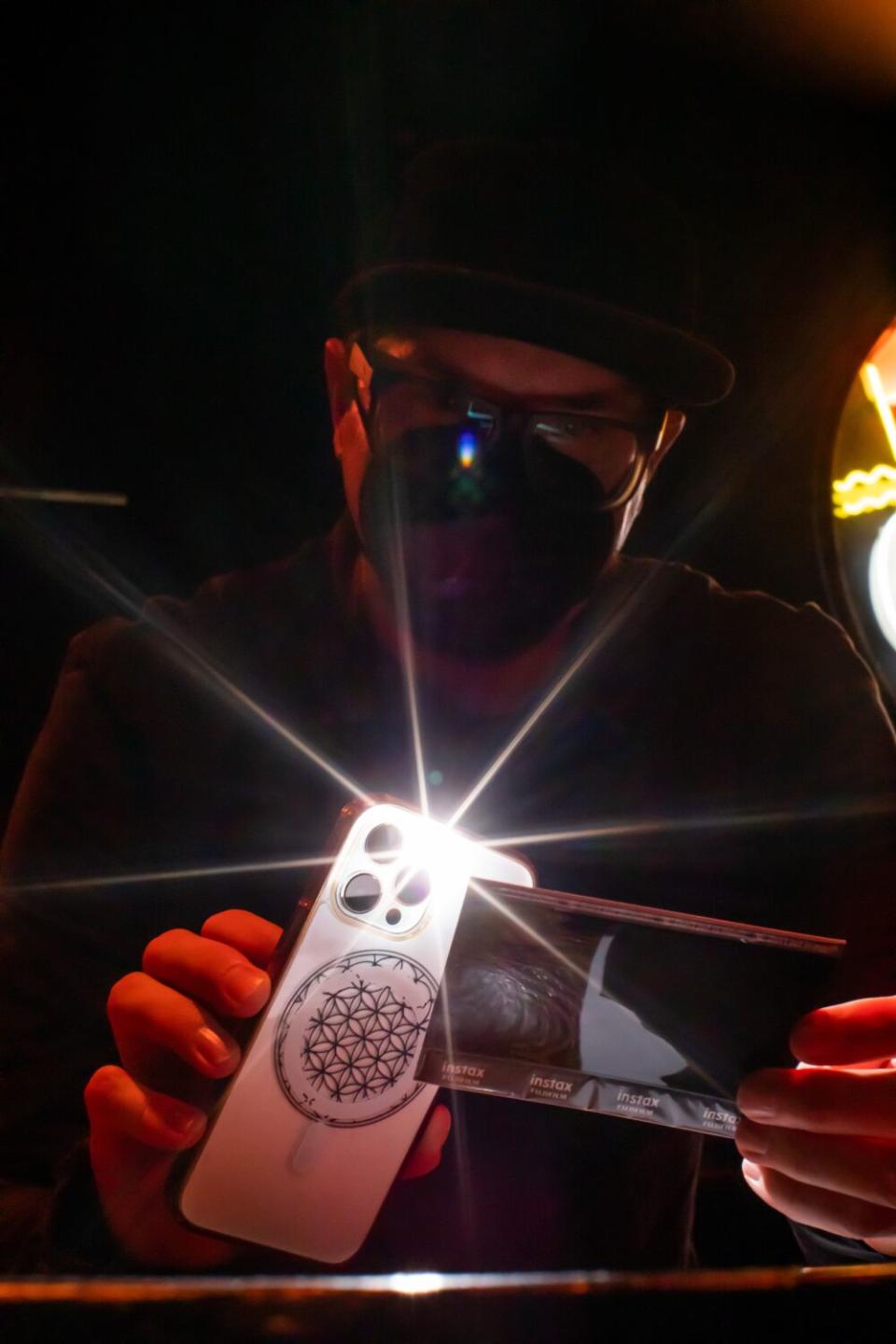 A man in a face mask shines a phone's light onto instant film