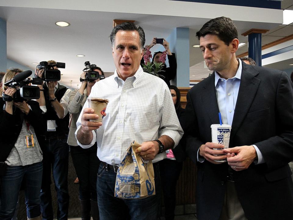 2012 Republican presidential nominee Mitt Romney carrying a bag of fast food with his running mate, Paul Ryan, while surrounded by reporters.